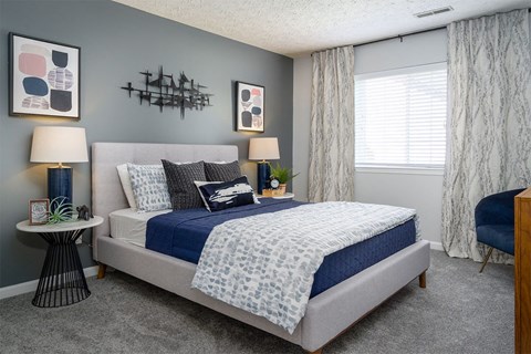 A bedroom with a bed, two lamps, a nightstand, and a chair.