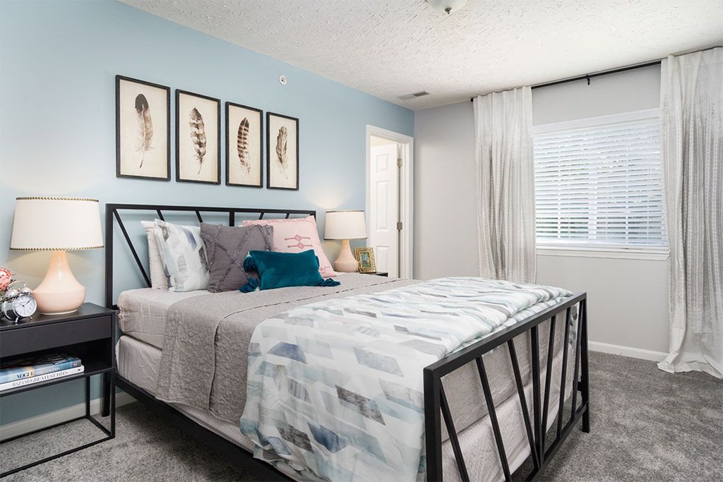 A bedroom with a bed, nightstand, and a window with curtains.
