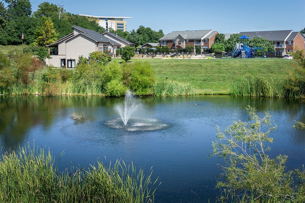 A fountain in the middle of a lake surrounded by greenery.