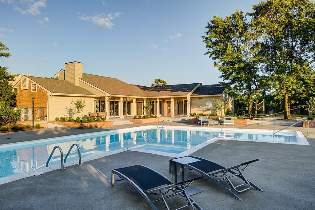 a swimming pool with two lounge chairs in front of a house