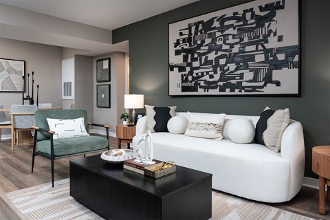 A living room with a white couch, a green chair, and a large abstract painting on the wall.