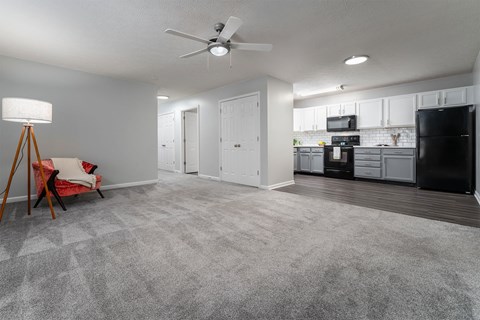 an empty living room with a kitchen and a ceiling fan