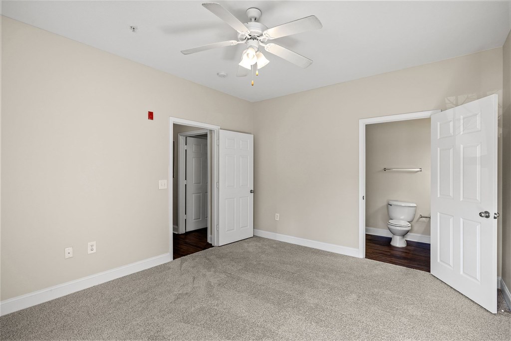 A room with a ceiling fan and a toilet in the corner.