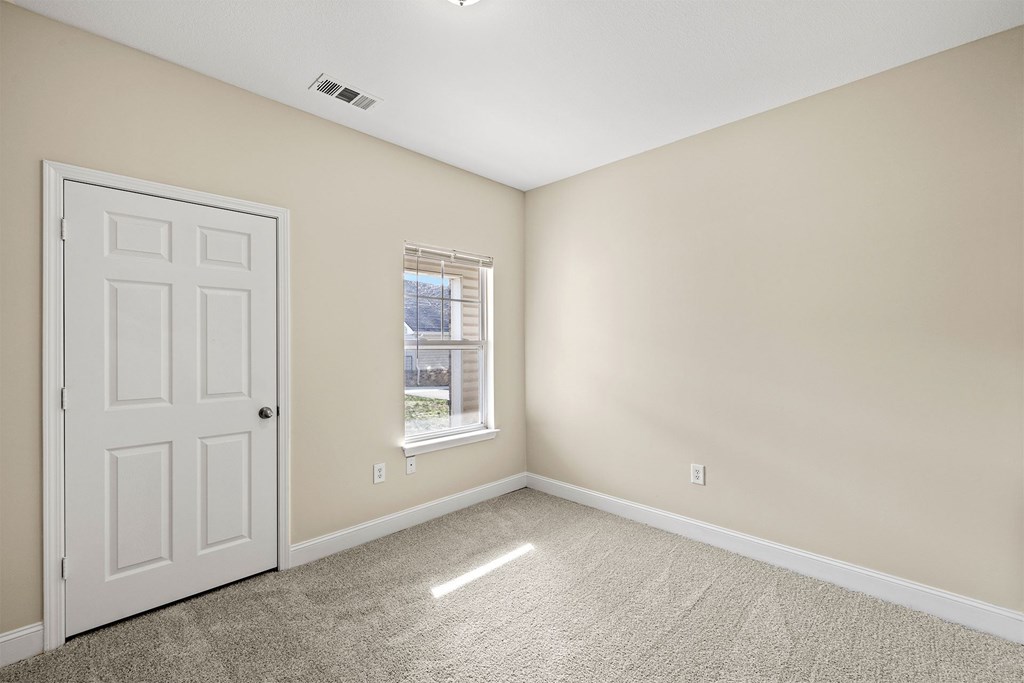 A room with a white door and a window with a view of a building outside.