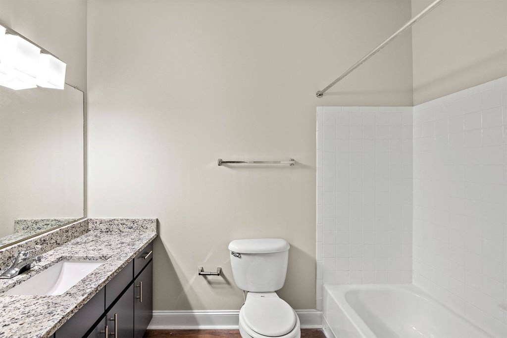 A white toilet sits in a bathroom next to a sink and a bathtub.