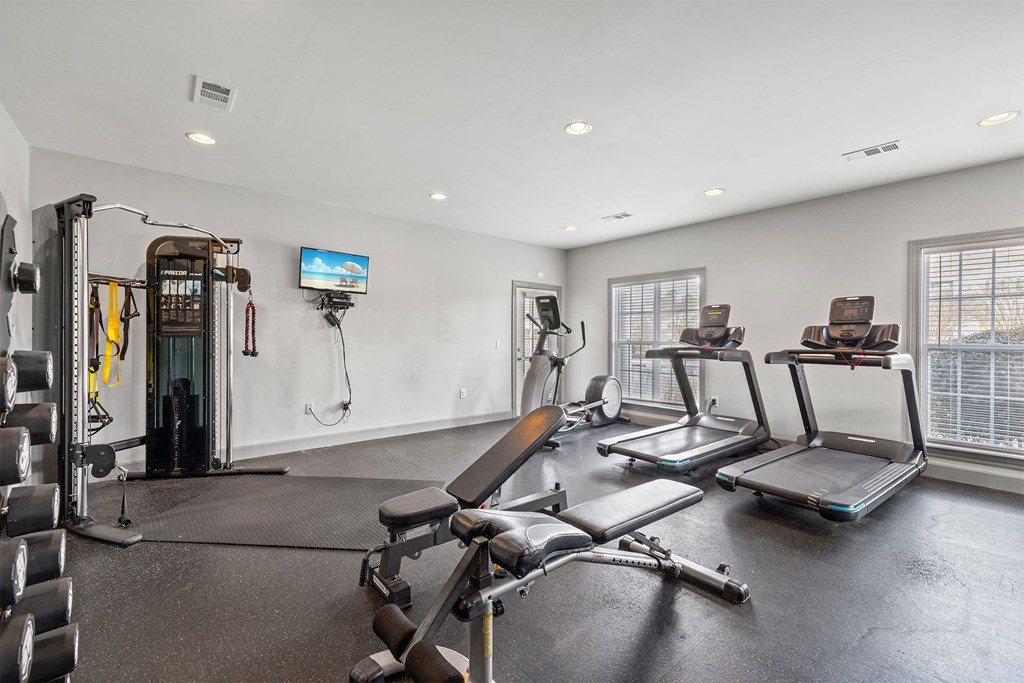 A home gym with a variety of equipment including a treadmill, weights, and a television.