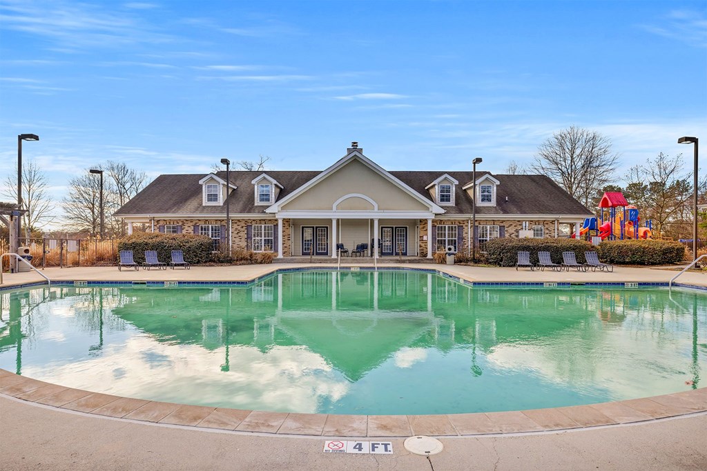 A large swimming pool in front of a building with a playground in the background.