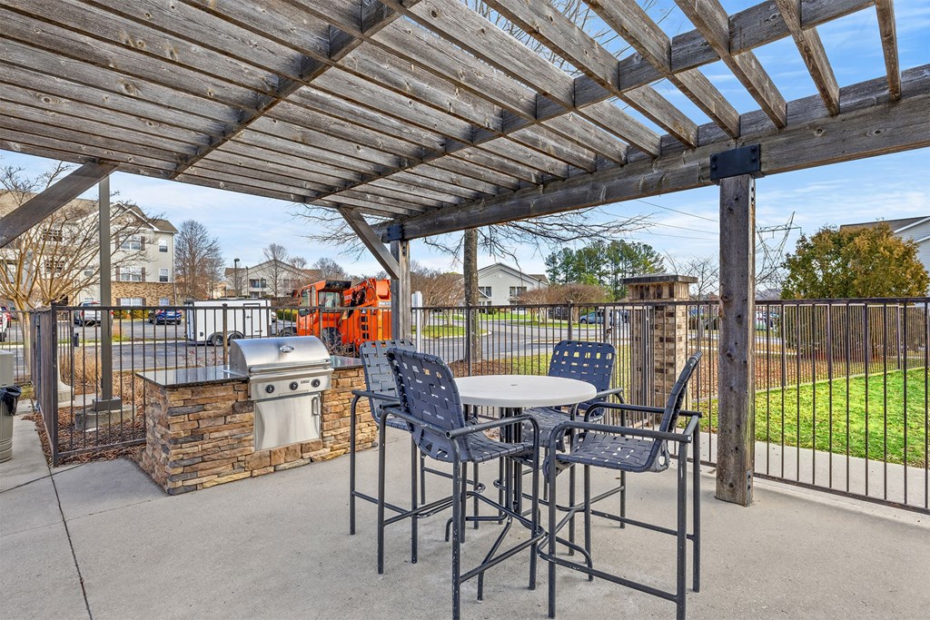A patio with a table and chairs under a wooden pergola.