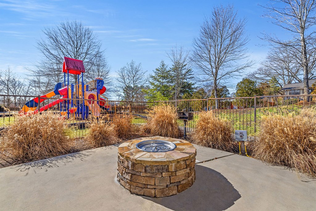 A playground with a red and blue slide and a circular stone structure in the middle.