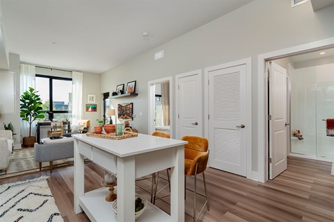 A white dining table with a basket of fruit on it and a yellow chair in front of it.