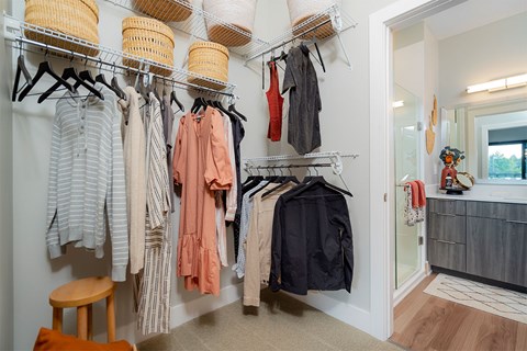 A room with a white wall and a wooden stool with clothes hanging on a rack.