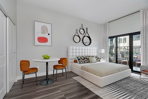 A bedroom with a white bed, a round table with two chairs, and a painting on the wall.