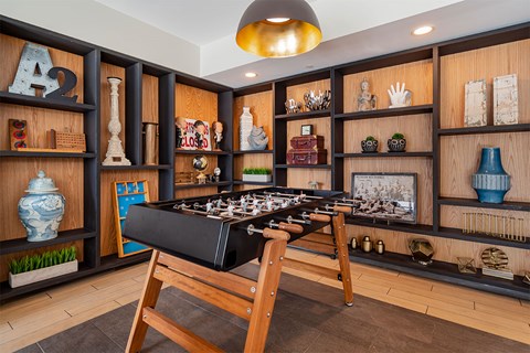 A chessboard is set up on a wooden table in a room with shelves filled with various objects.