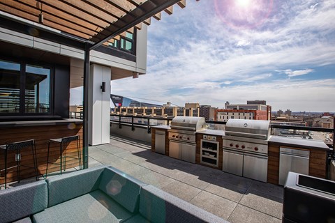 A rooftop patio with a grill and bar stools.