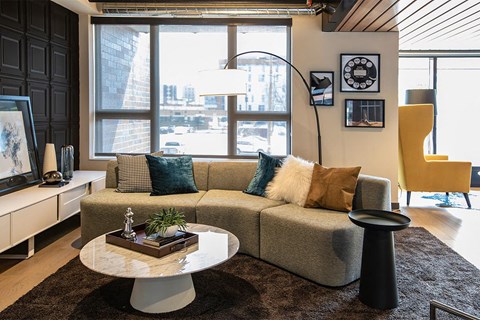 A modern living room with a grey couch, a round table, and a large window.