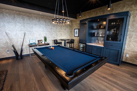 A pool table is in the middle of a room with a dark wood floor and a patterned wall.