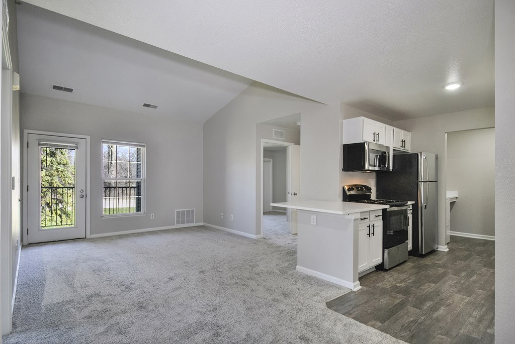 an empty living room with a kitchen with a stove and refrigerator