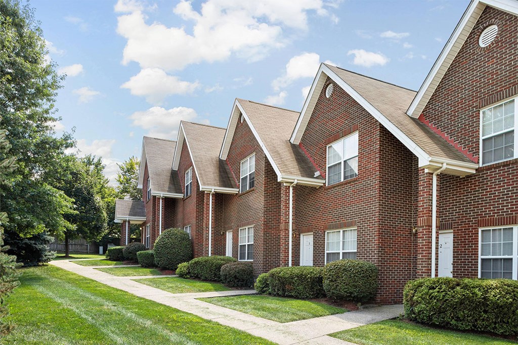 a row of brick apartment buildings with a sidewalk and grass