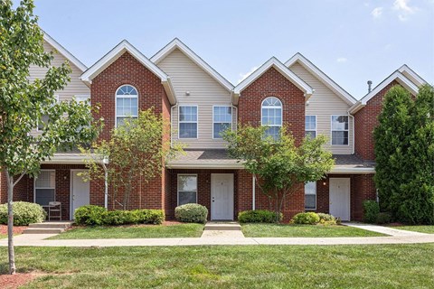 front view of two story brick and white home with grass and trees