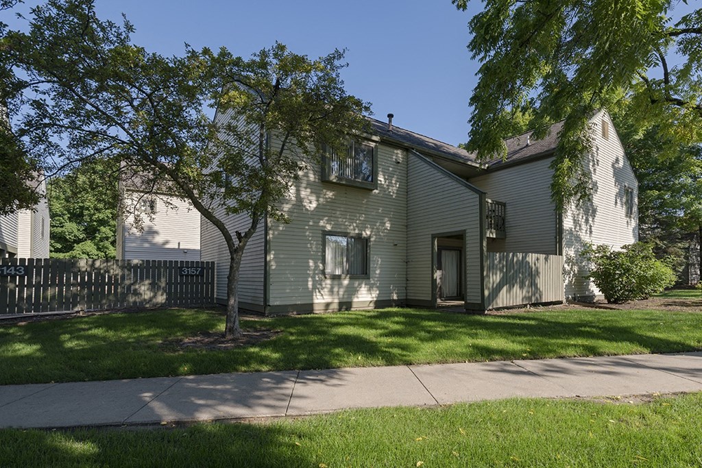 a green house with a sidewalk and trees in front of it