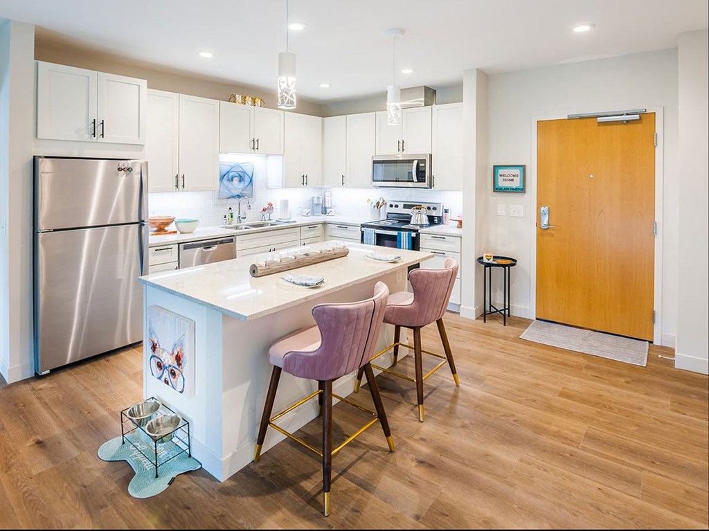A kitchen with a white island and pink chairs.