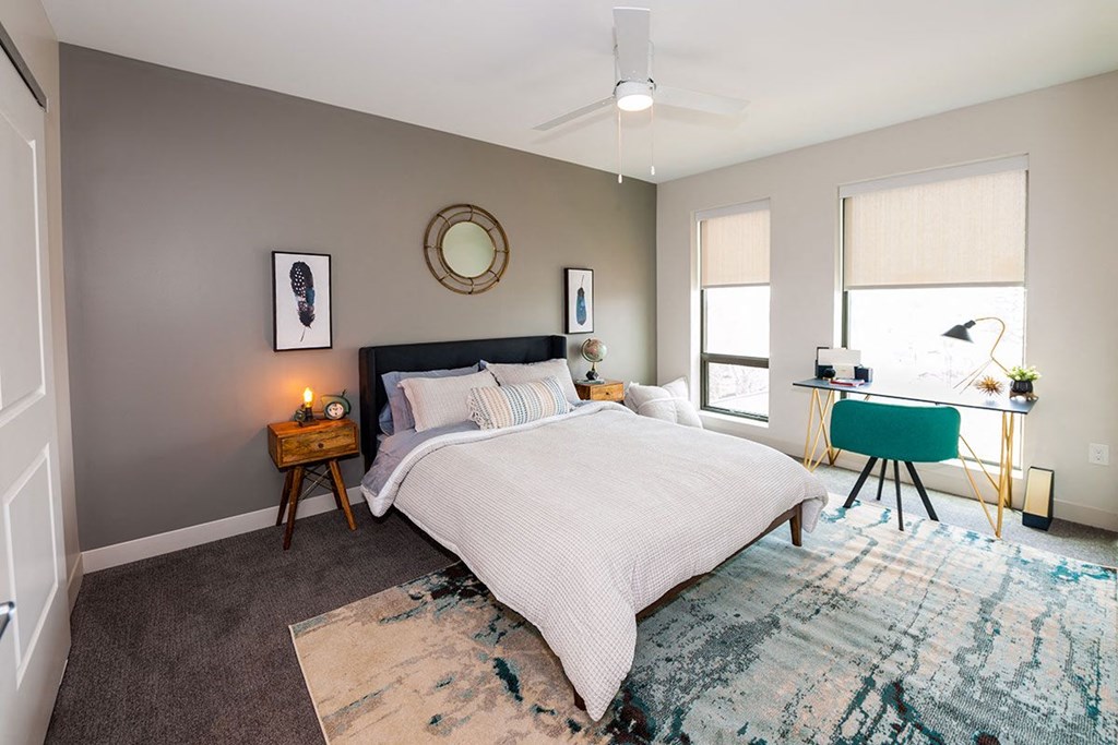 A bedroom with a large bed, a desk with a chair, and a rug on the floor.