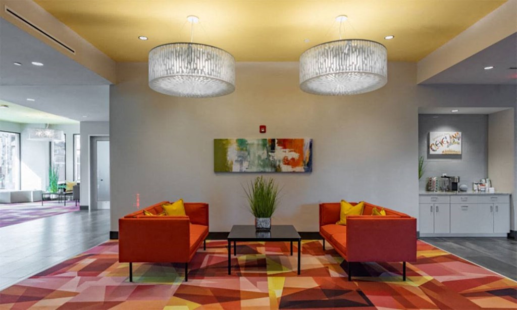 A brightly colored lobby with two orange couches and a large painting on the wall.
