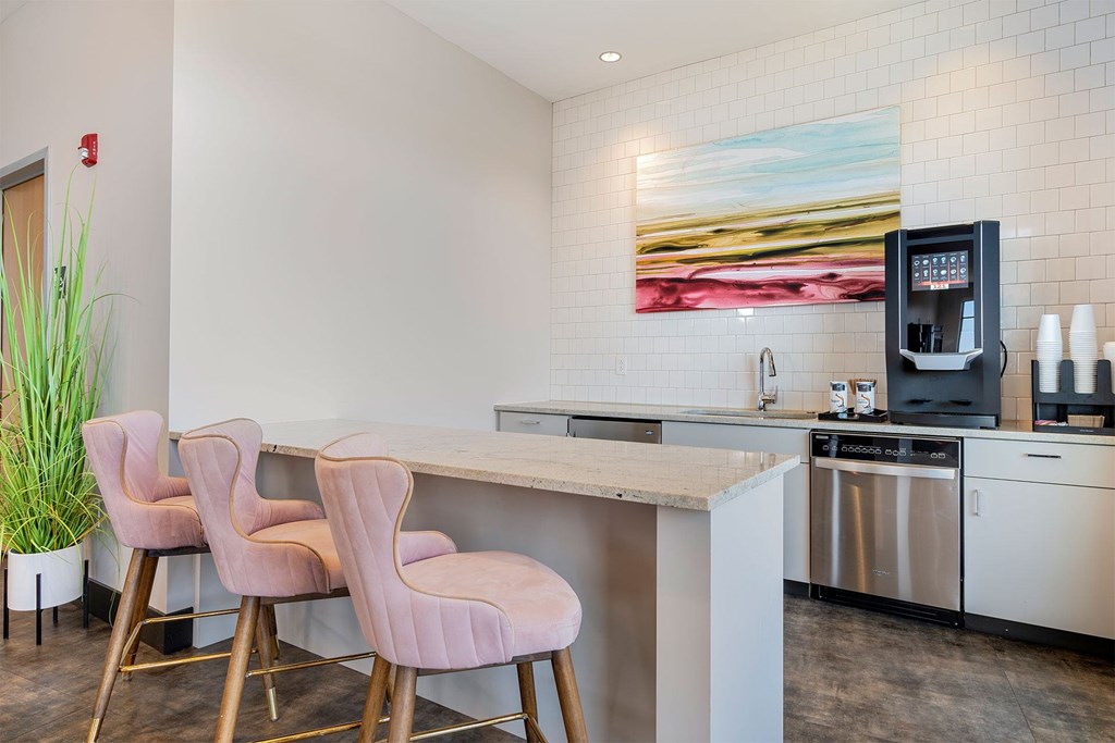 A kitchen with a bar area and pink chairs.