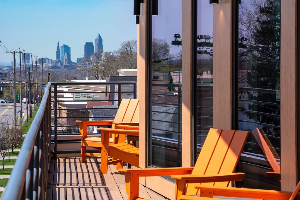 Two orange chairs on a balcony overlooking a city skyline.