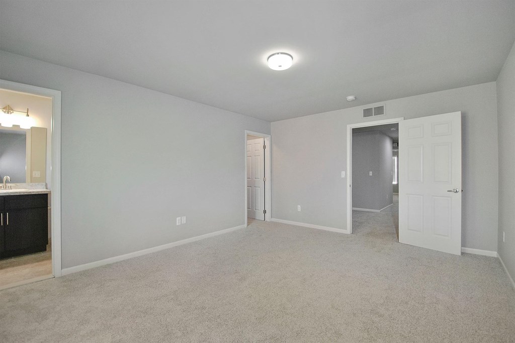an empty living room with white carpet and a door to a hallway