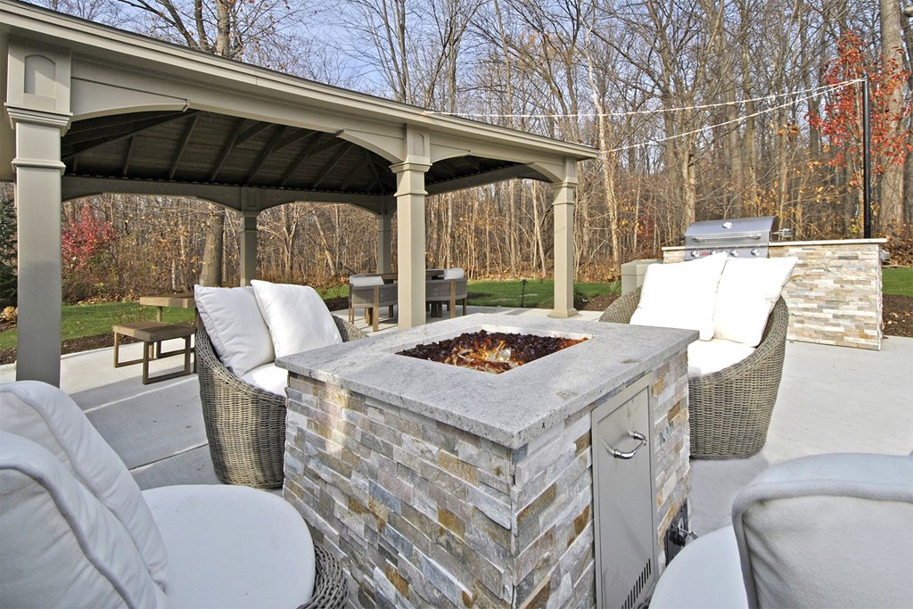 a patio with a fire pit and chairs and a roof
