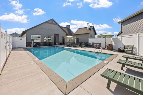 A pool with a bench and a table with chairs is surrounded by a fence.