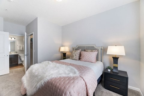 A bedroom with a bed covered in a pink comforter and a white fur throw.