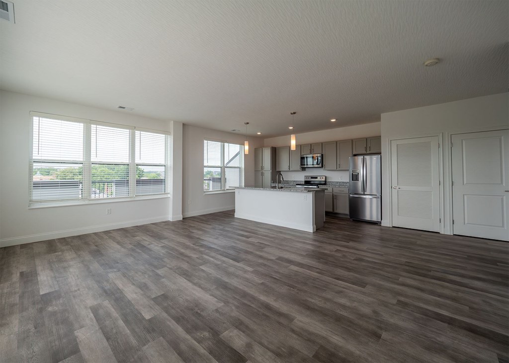 A spacious room with wooden flooring and a kitchen area in the background.