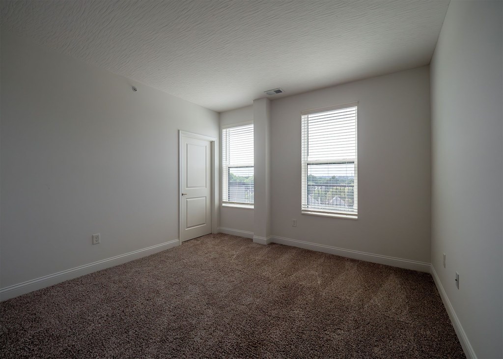 A room with carpeted floor and two windows.