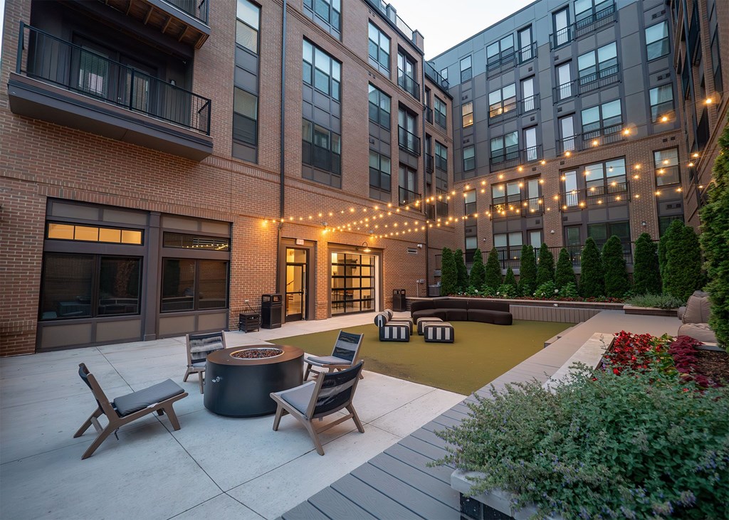 A patio with a fire pit and chairs is surrounded by buildings.