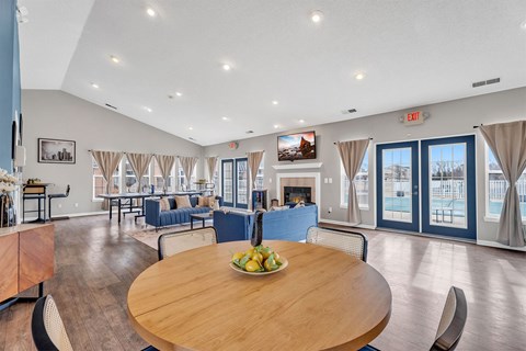 A large room with a wooden table and chairs in the foreground and a pool in the background.