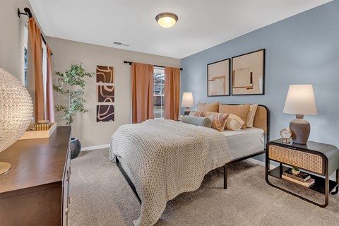 A bedroom with a bed, nightstand, and a plant.