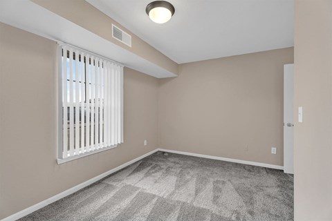 A room with a carpeted floor and a window with blinds.