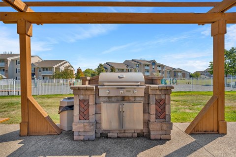 A BBQ grill is under a wooden pergola in a suburban setting.