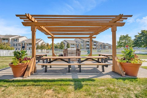 A wooden pergola with benches and potted plants in the foreground with apartment buildings in the background.