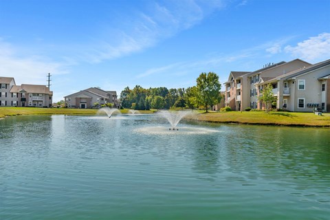 A fountain in the middle of a lake in front of apartment buildings.