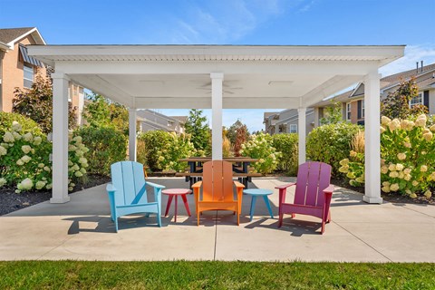 A white pergola with four chairs and two tables in front of a building.