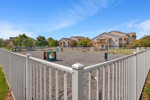 A white fence surrounds a playground and houses in the background.