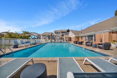 A large swimming pool with lounge chairs and a building in the background.