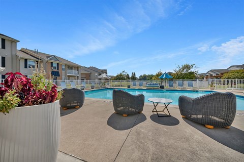 A pool area with chairs and a table with a vase of flowers in the foreground.