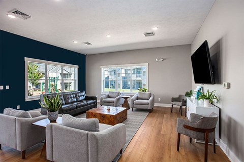 A living room with a black couch, grey armchairs, a wooden coffee table, and a flat-screen TV mounted on the wall.