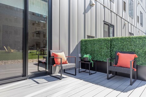 a patio with two chairs and a table and a green hedge