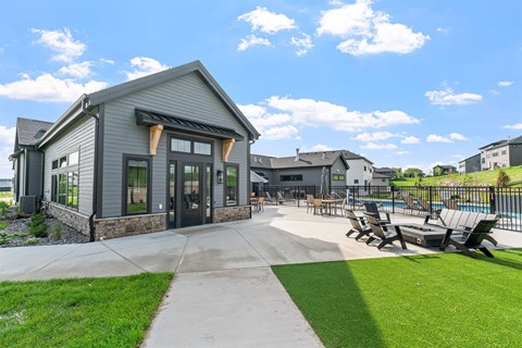 A modern building with a grey exterior and a black roof is surrounded by a grassy area and a concrete walkway.