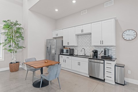 A kitchen with a table and chairs in the foreground and a refrigerator, microwave, and oven in the background.